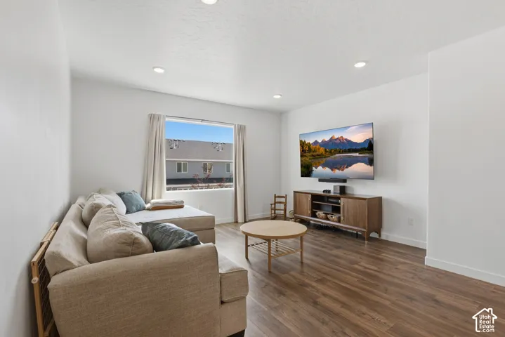 Bright, open-concept living area featuring recessed ceiling lighting, wood-finish flooring throughout, and large windows framed with neutral drapery