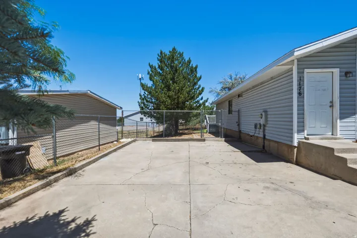 Paved concrete driveway with chain-link fencing, mature tree, and exterior siding