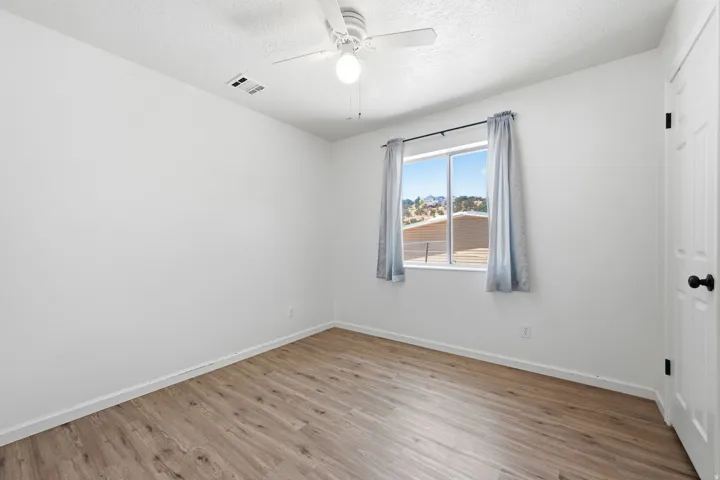 Wood-finish flooring with white baseboards, bright white walls, and a window with a distant landscape