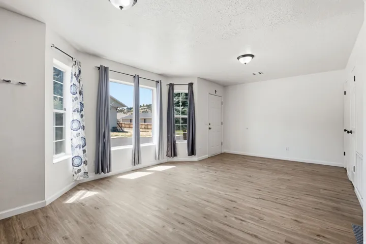 Wood-finish flooring throughout, multiple windows with white trim, white walls, and a front entry door with a black handle