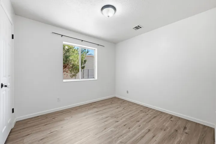 Wood-finish flooring, white painted walls, and a single window with black hardware