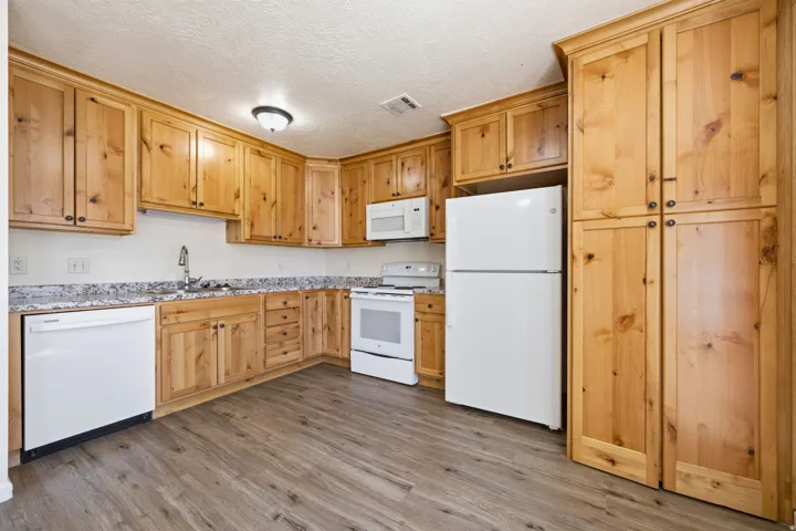 Kitchen featuring wood-finish cabinetry, granite-style countertops, wood-finish flooring, and white appliances