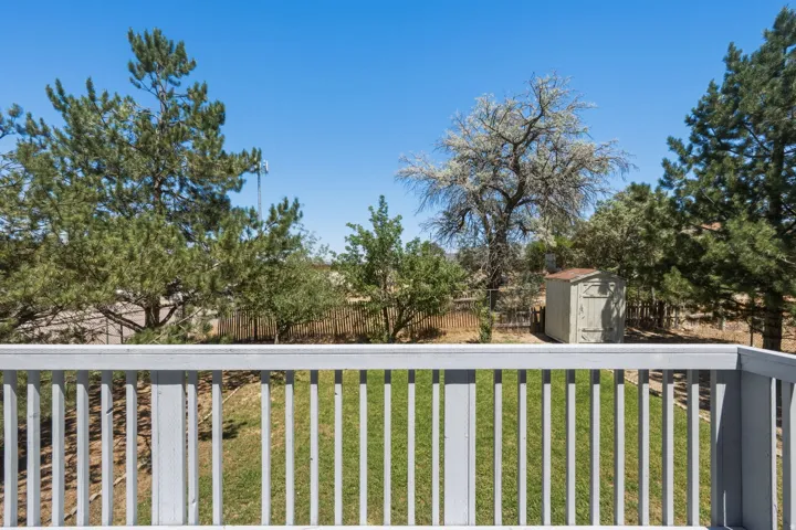 Expansive outdoor space featuring a painted wood railing, a storage shed, mature trees, and a clear blue sky
