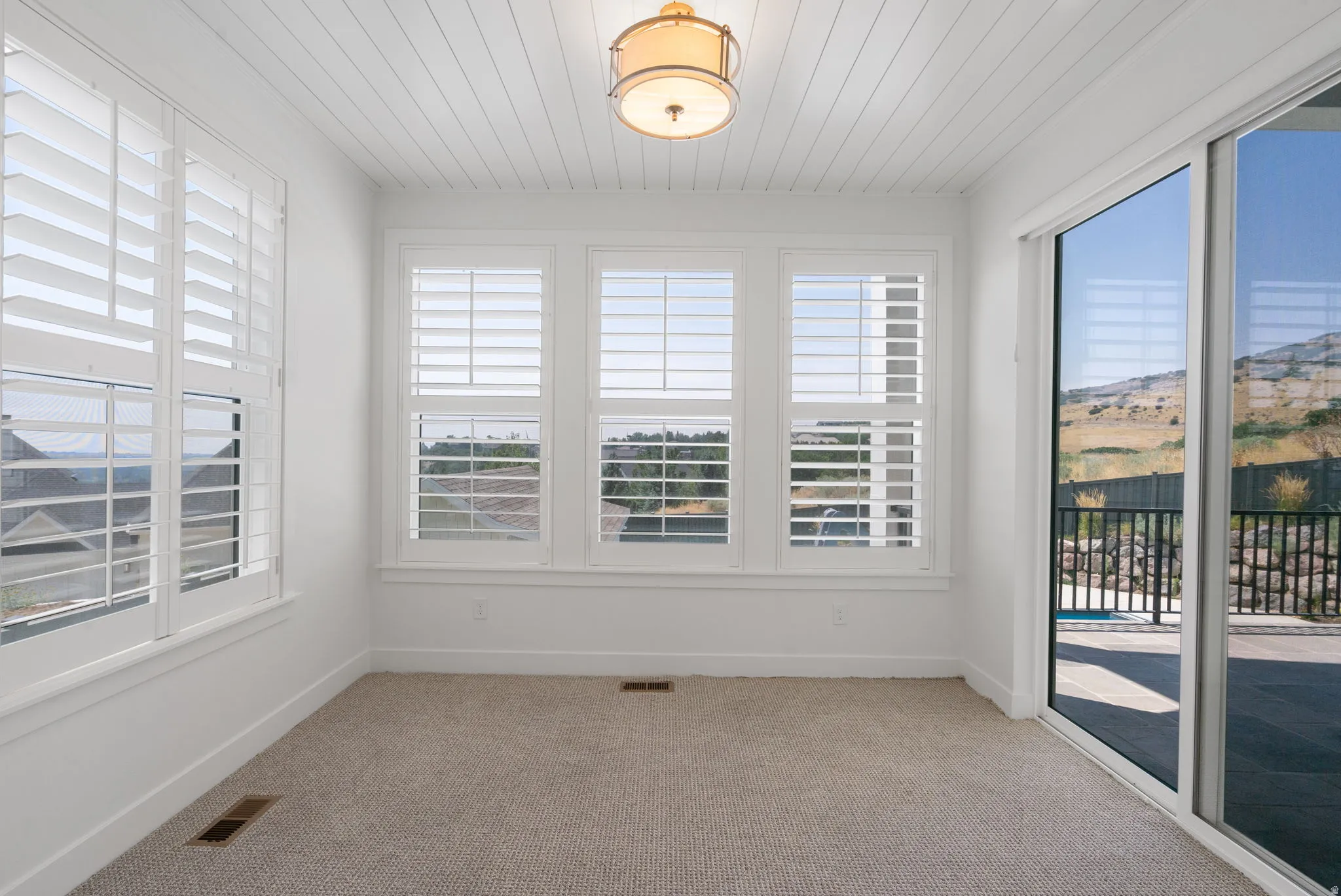 Carpeted interior with multiple windows featuring white plantation shutters, white paneled ceiling, and a ceiling-mounted light fixture