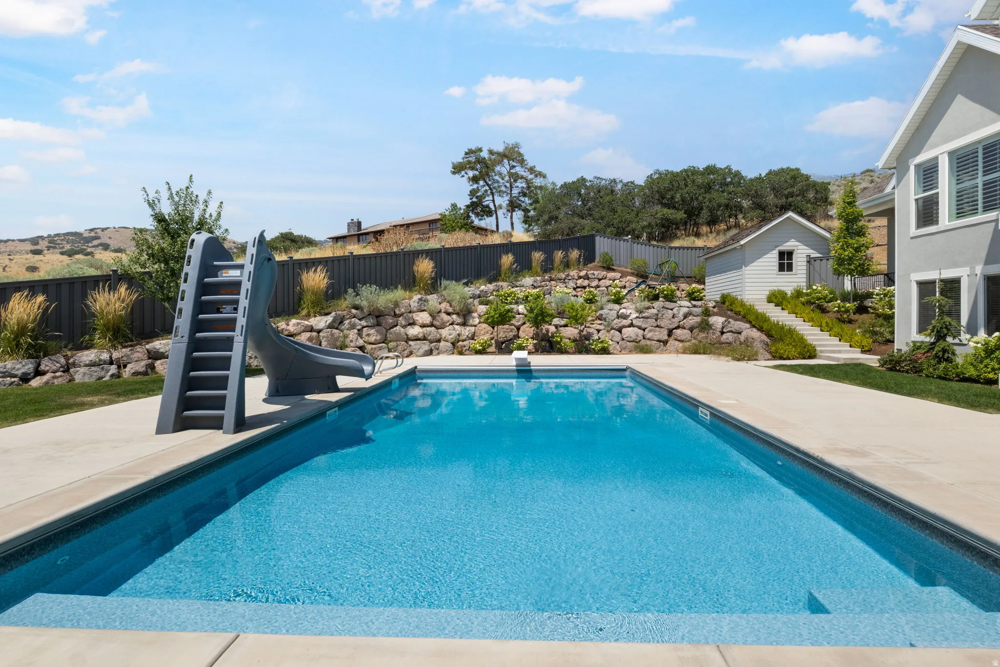 Outdoor swimming pool with integrated steps, concrete surround, adjacent slide, and terraced landscaping
