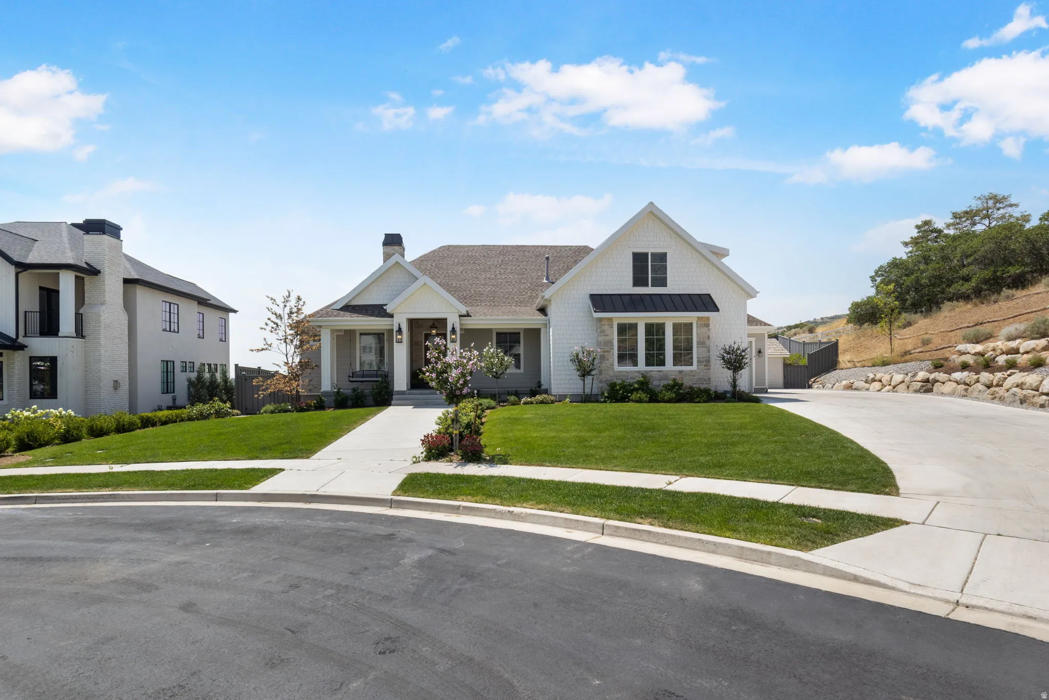 White siding exterior with black accents, covered porch entry, stone facade elements, front-facing gables, and an attached garage
