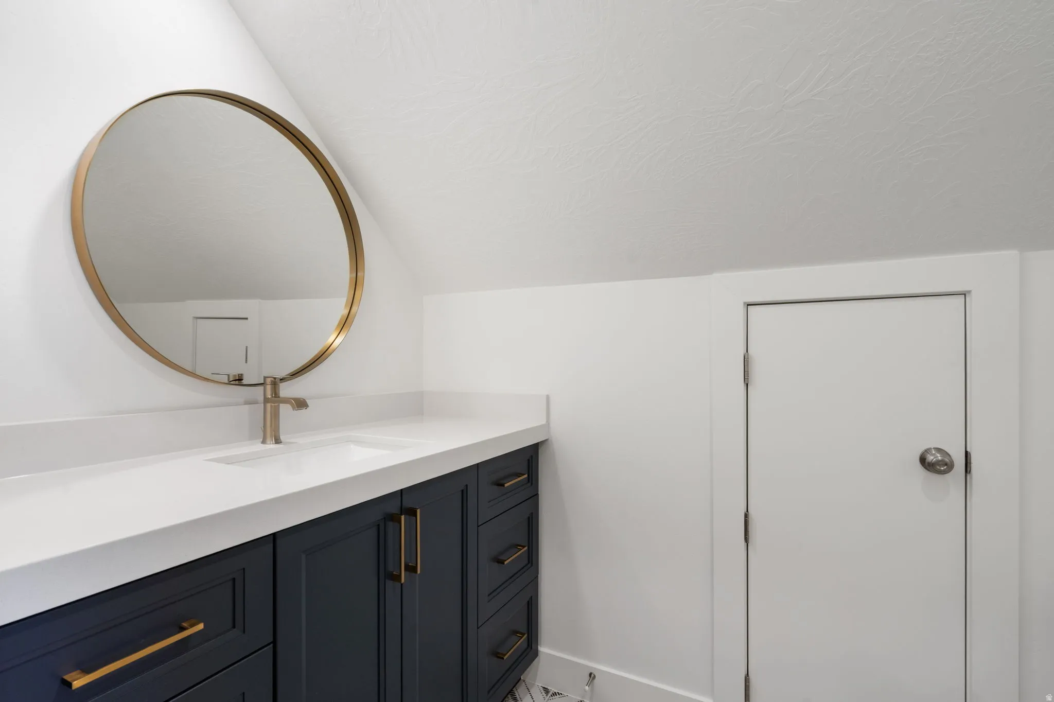 Vanity with a white countertop and integrated sink, gold-tone faucet, and dark blue cabinetry with gold-tone hardware