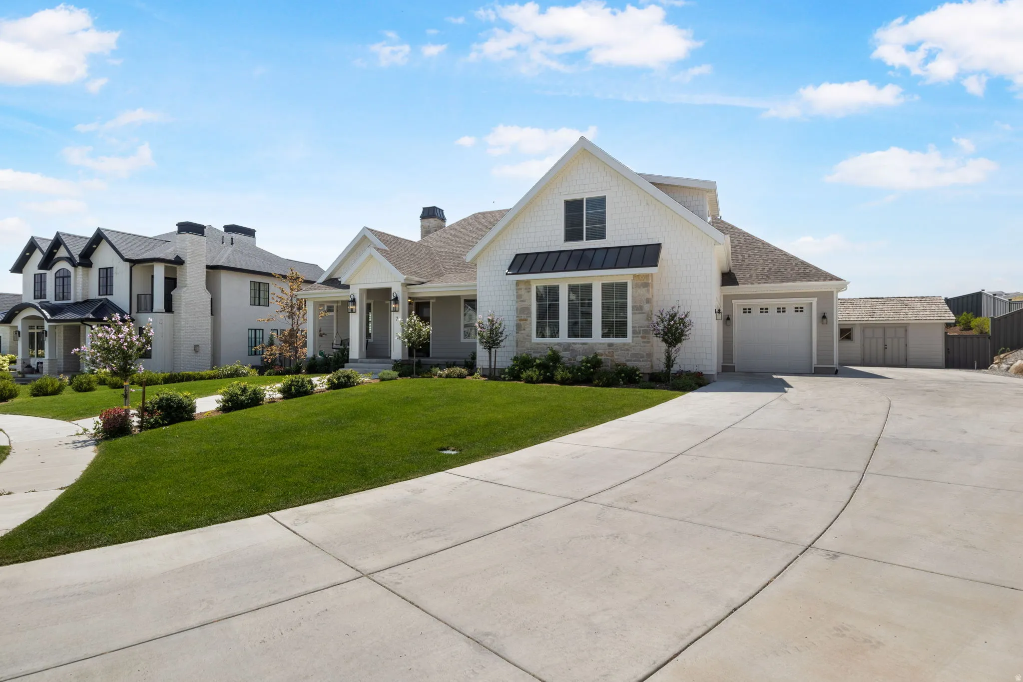 White siding exterior with a partial stone facade, a two-car garage, a concrete driveway, and a manicured lawn