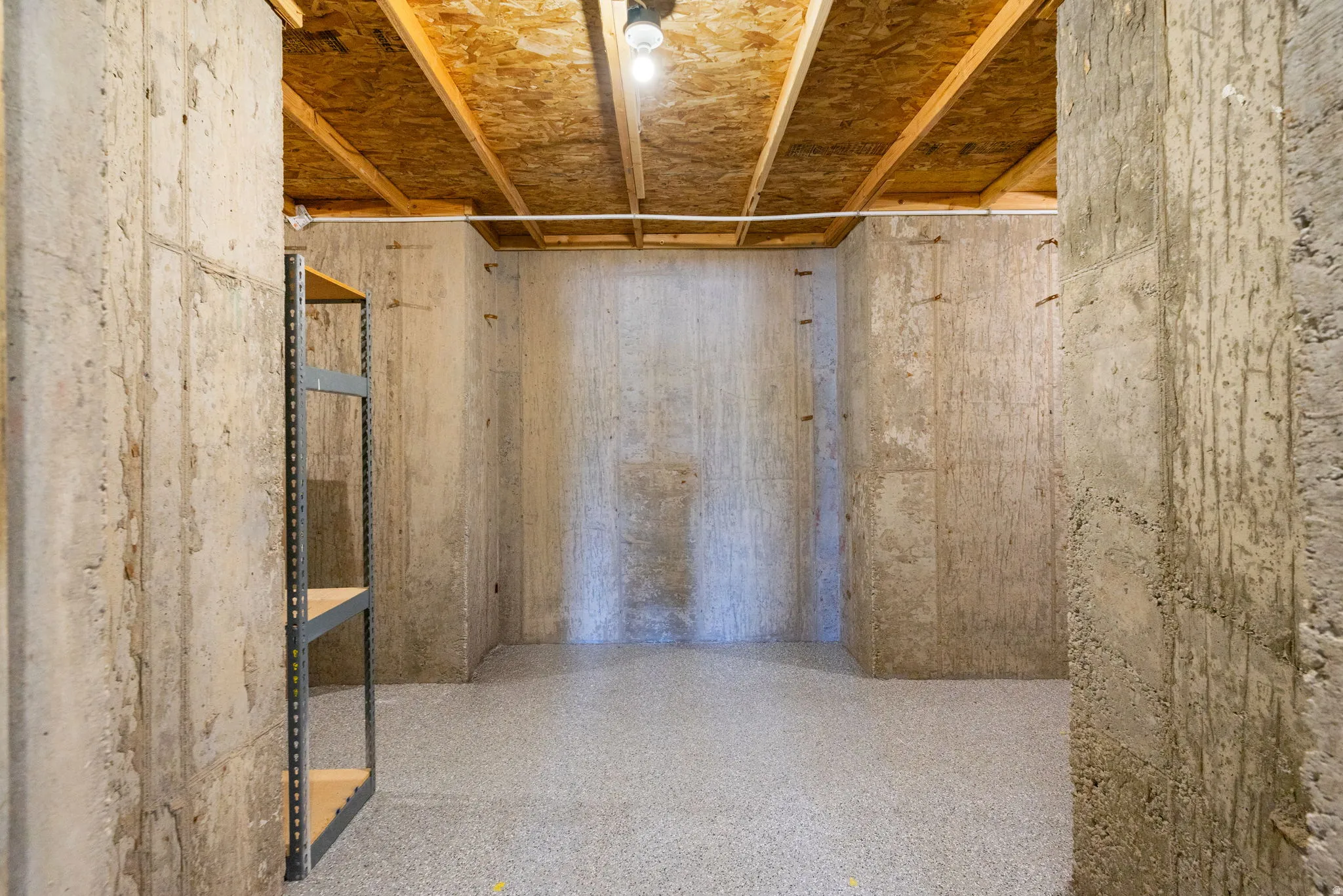 Exposed concrete walls with wood beam ceiling and a light-colored speckled flooring