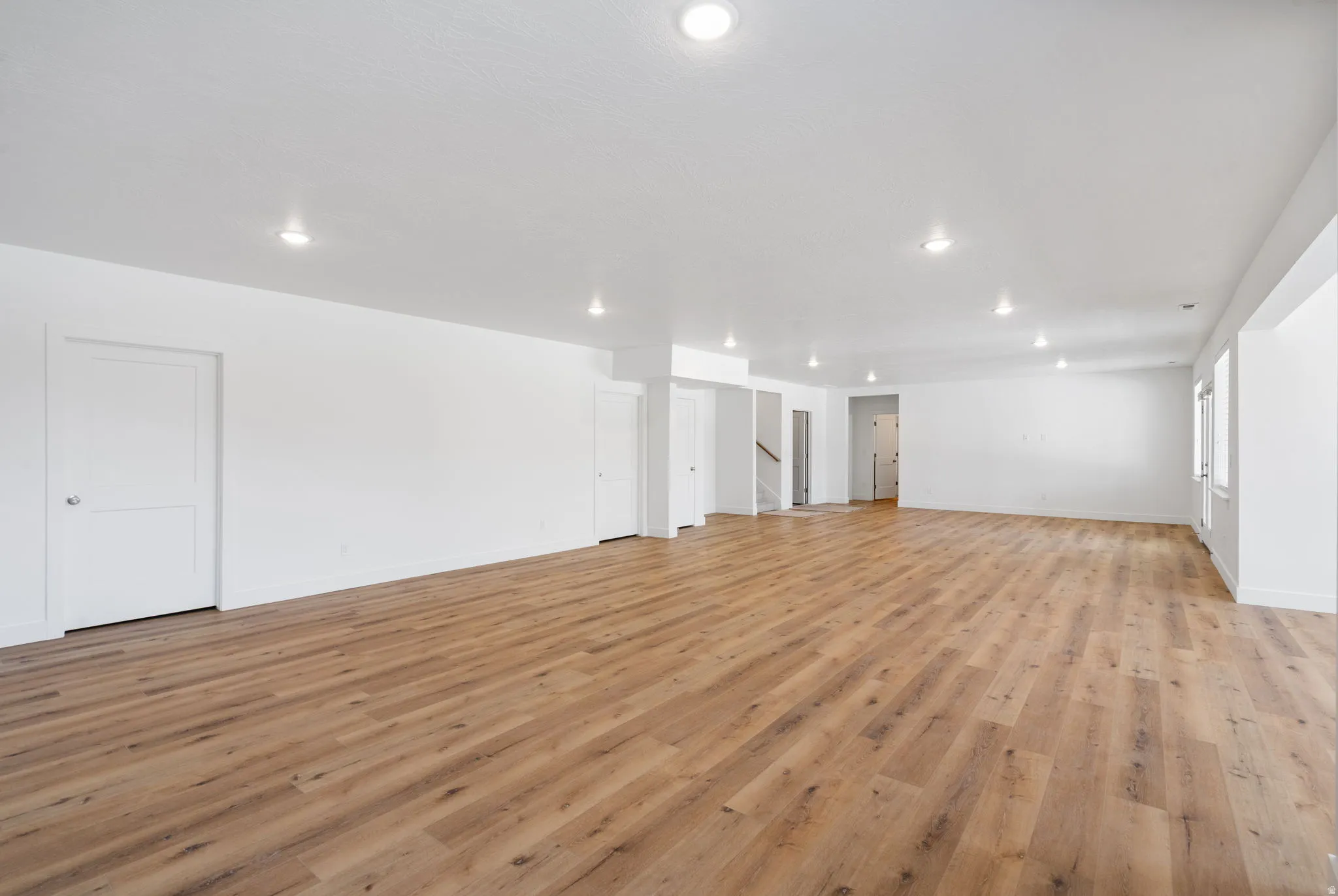 Spacious room featuring wood-finish flooring, white walls, recessed lighting, and multiple windows