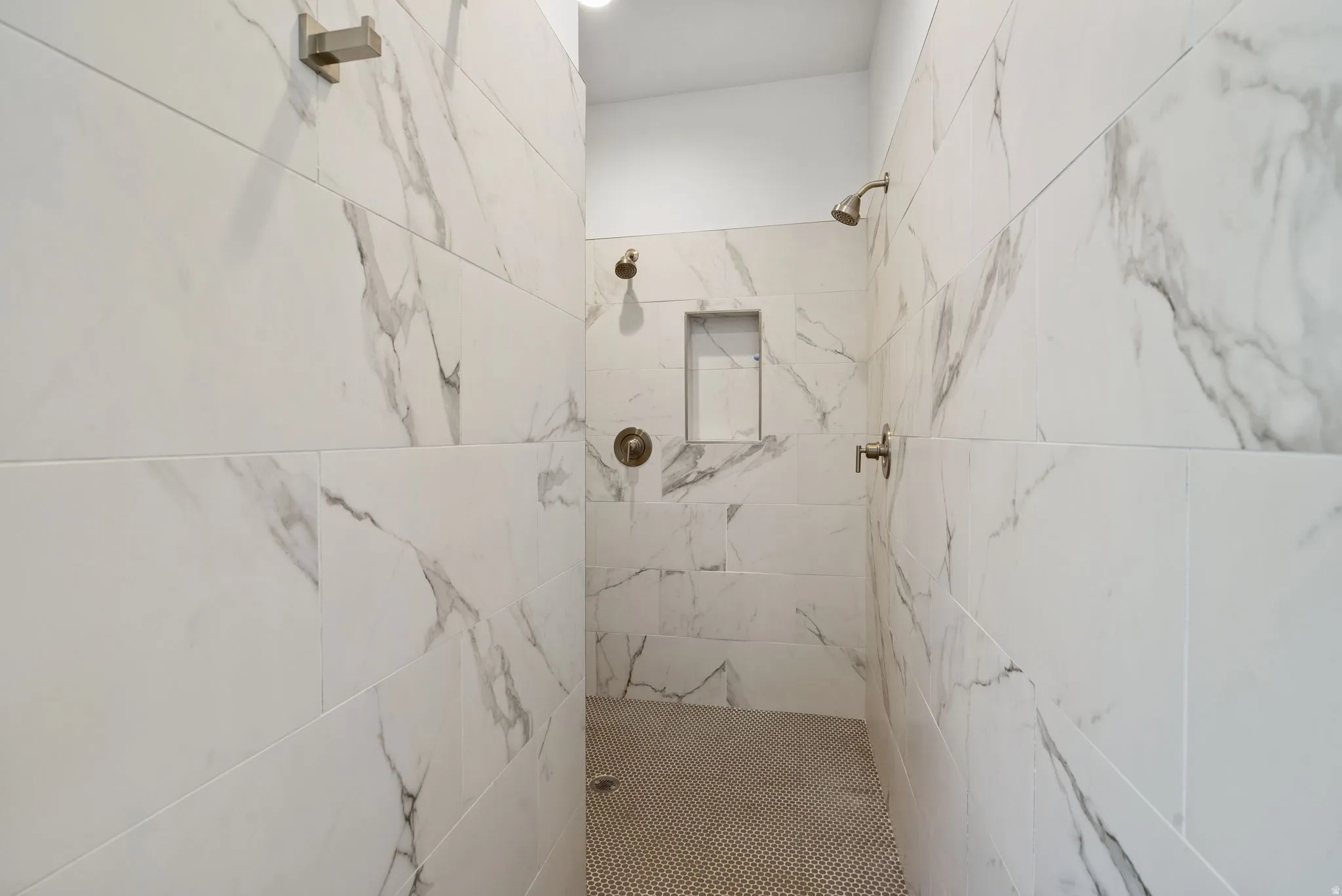 Shower enclosure with large format stone-finish tile, dual shower heads, integrated wall niche, and mosaic tile flooring