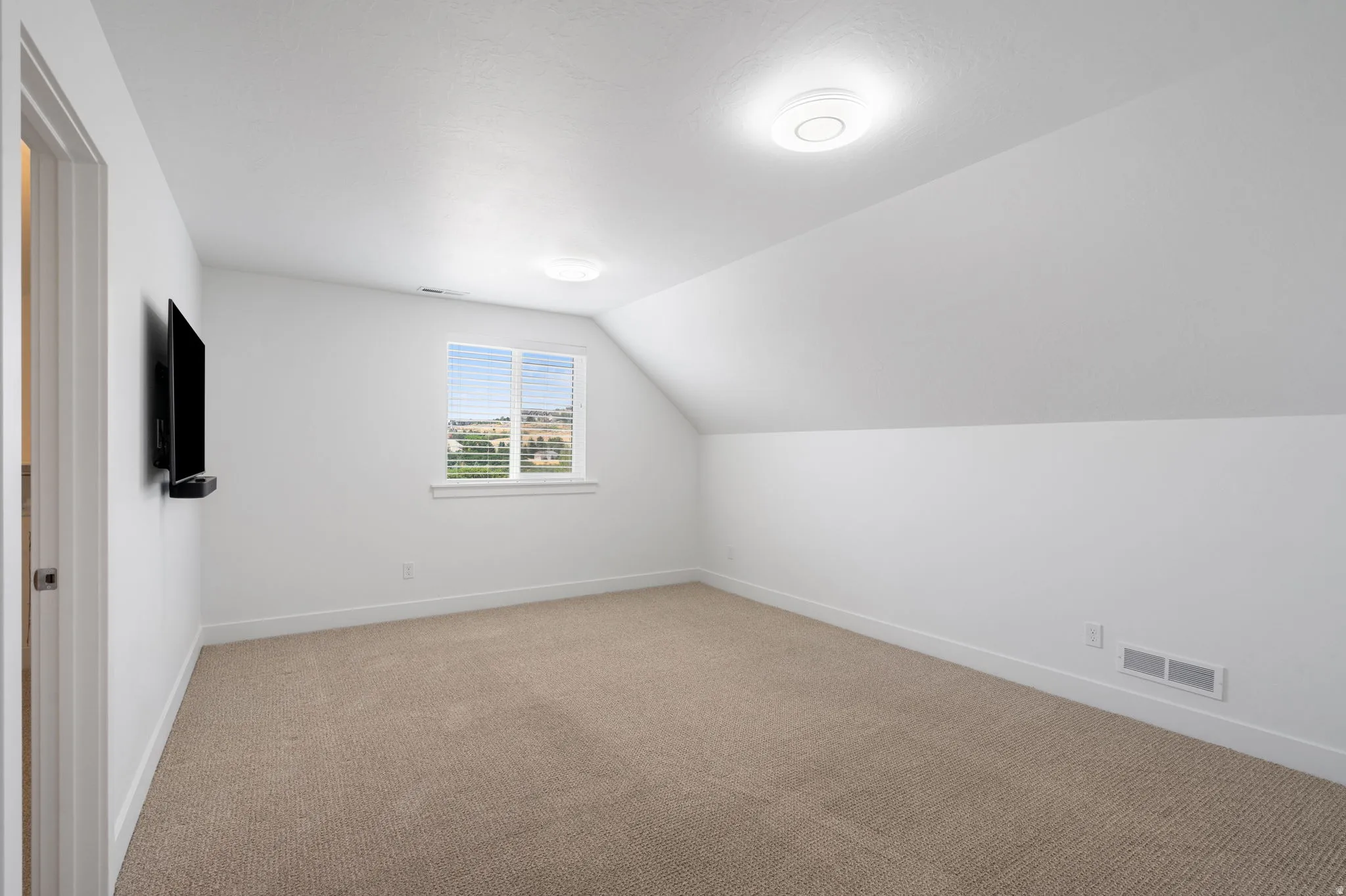 Carpeted room with a window, sloped ceiling, and flush-mount lighting fixtures