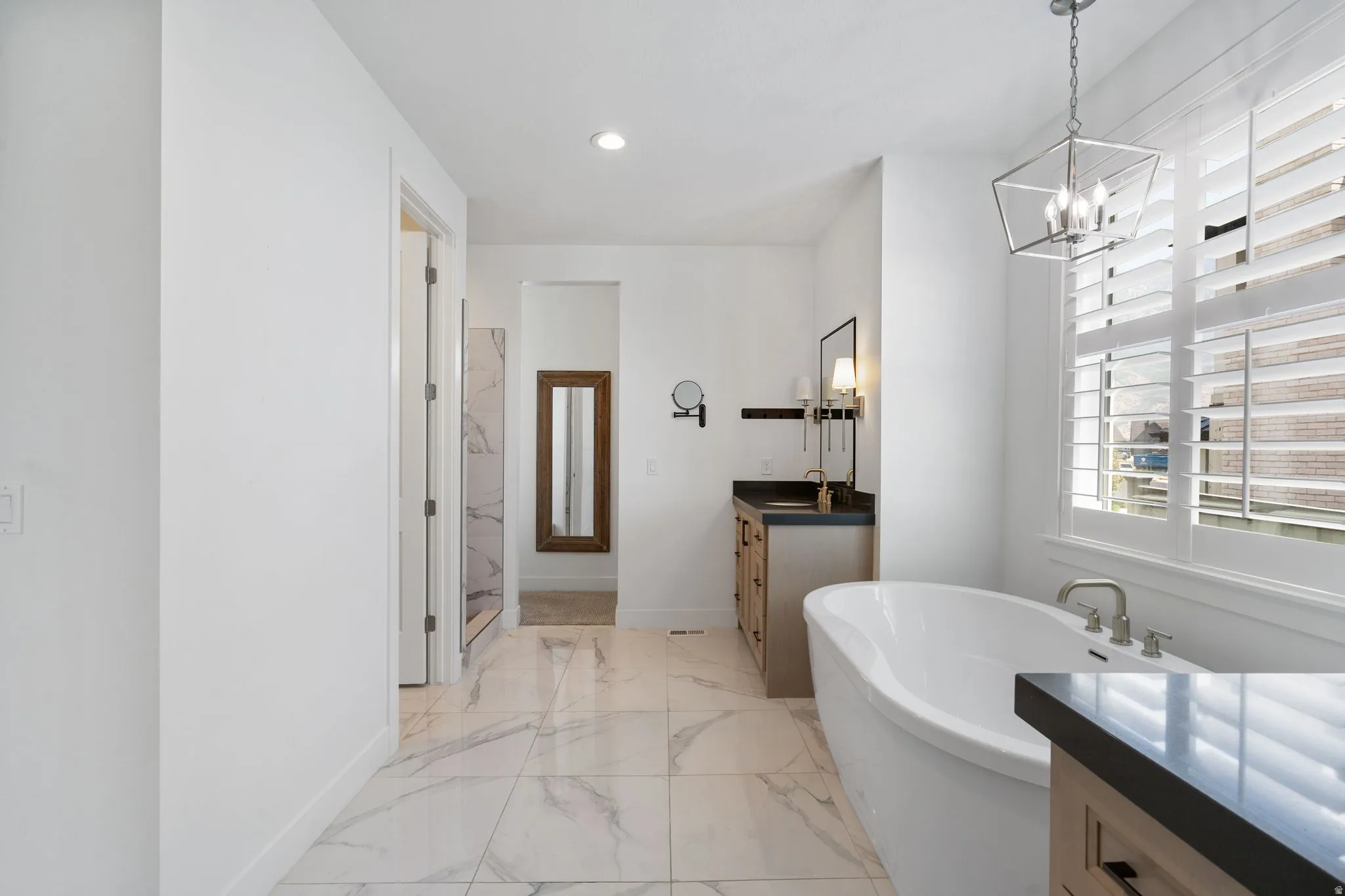 Freestanding soaking tub, walk-in shower with tile surround, double vanity with dark countertops, and large format floor tiling
