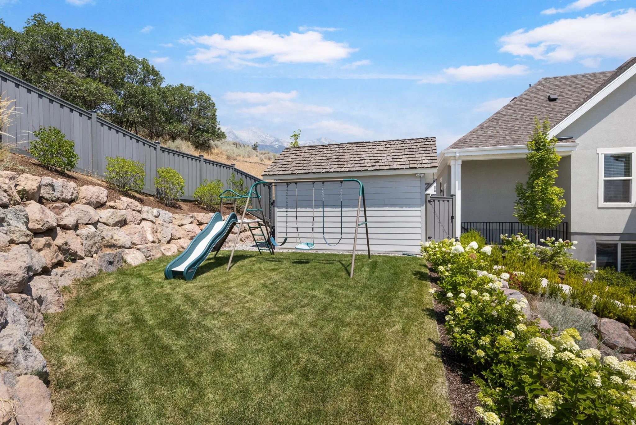 Expansive backyard featuring a rock retaining wall, manicured lawn, and mature landscaping