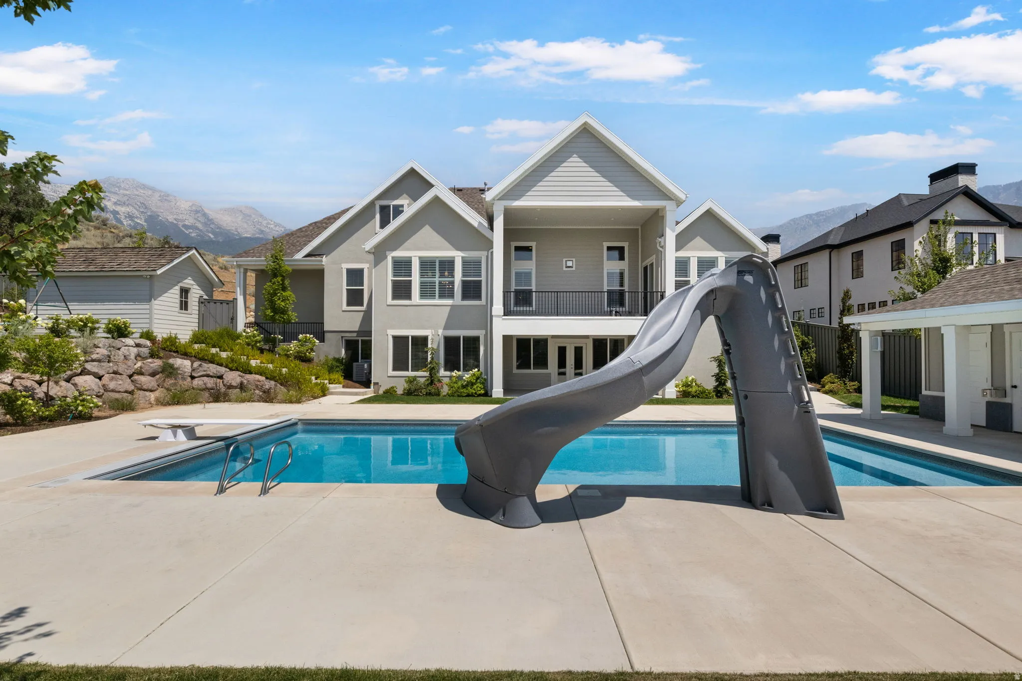Expansive backyard featuring an in-ground swimming pool with an attached slide, a diving board, and a surrounding concrete patio