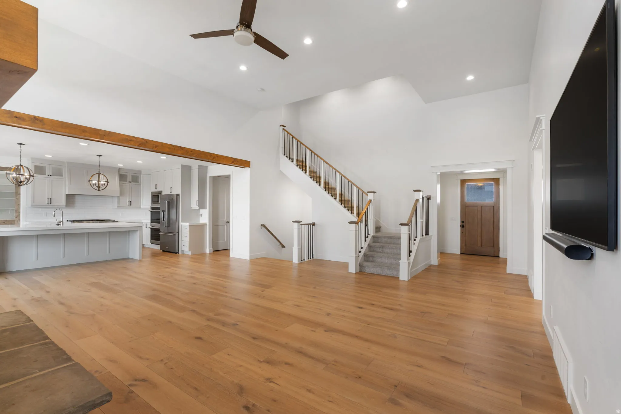 Soaring vaulted ceiling, recessed lighting, wood-finish flooring, staircase with wood handrails, and kitchen with stainless steel appliances