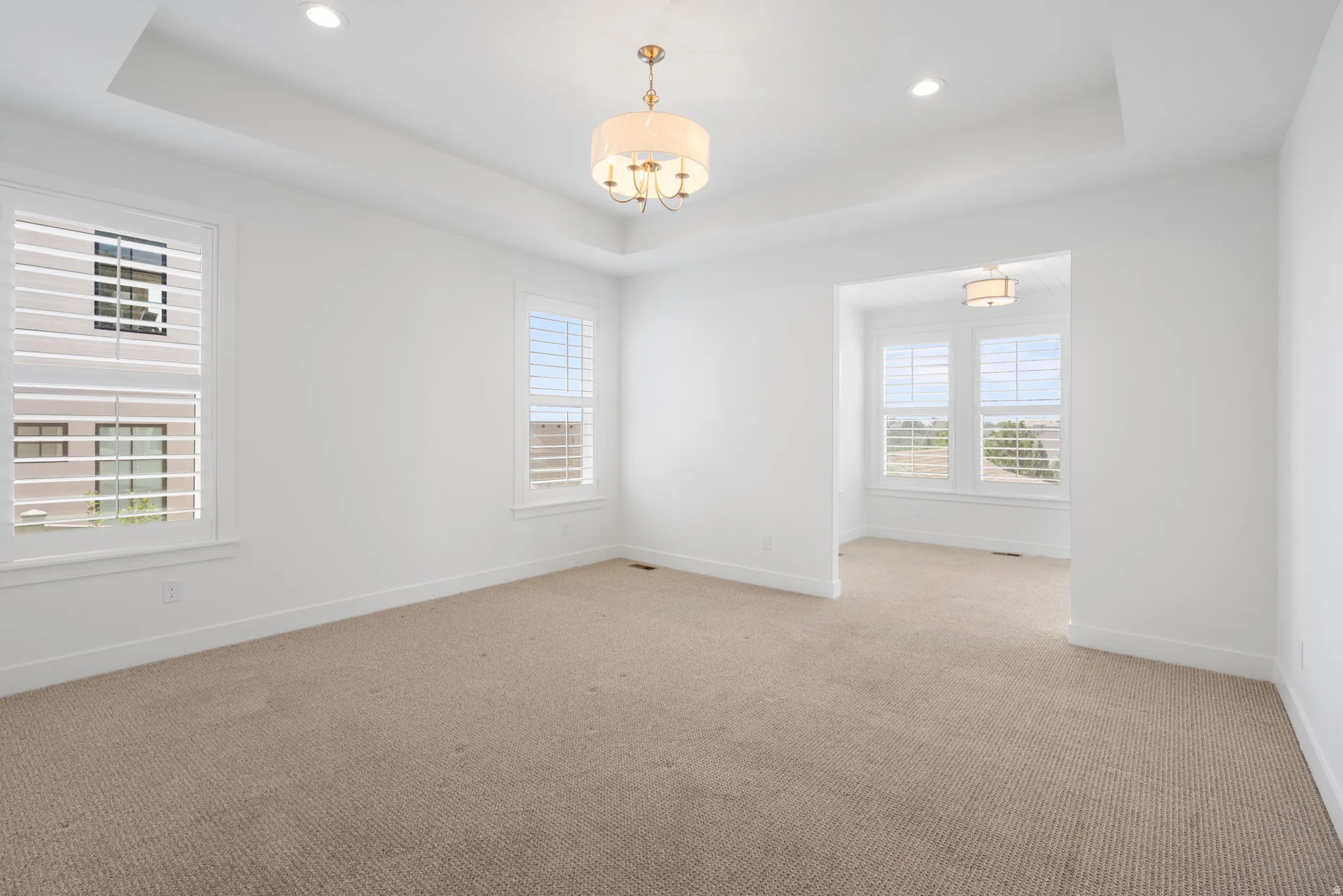 Recessed lighting, tray ceiling, chandelier, plantation shutters, and an arched entryway
