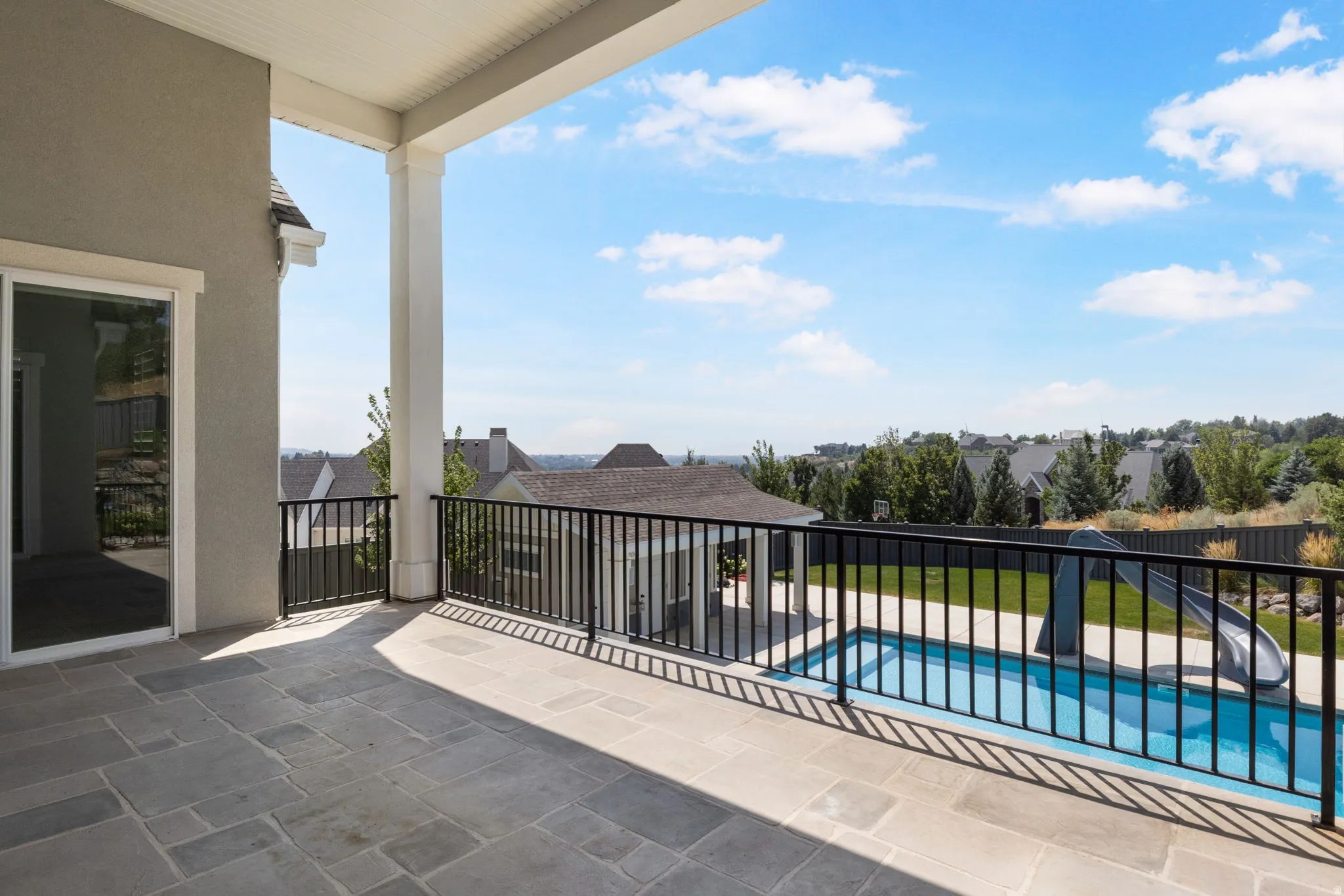 Covered patio featuring stone tile flooring, white support columns, and a black metal railing
