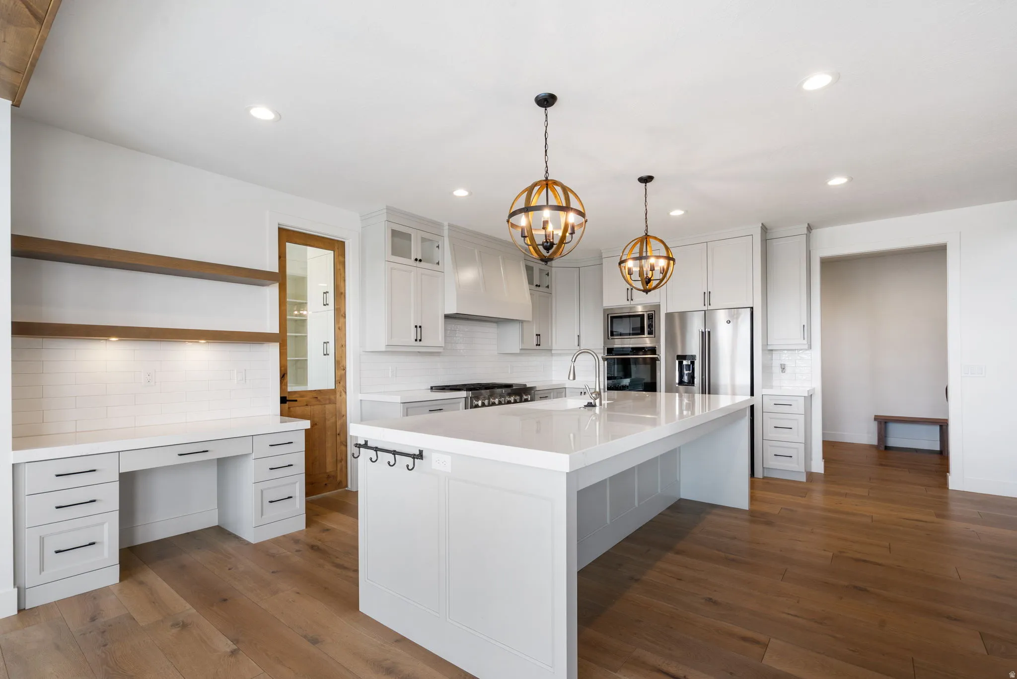 Spacious kitchen featuring an expansive island with a white countertop, built-in stainless steel appliances, white shaker cabinetry, and wood-finish flooring