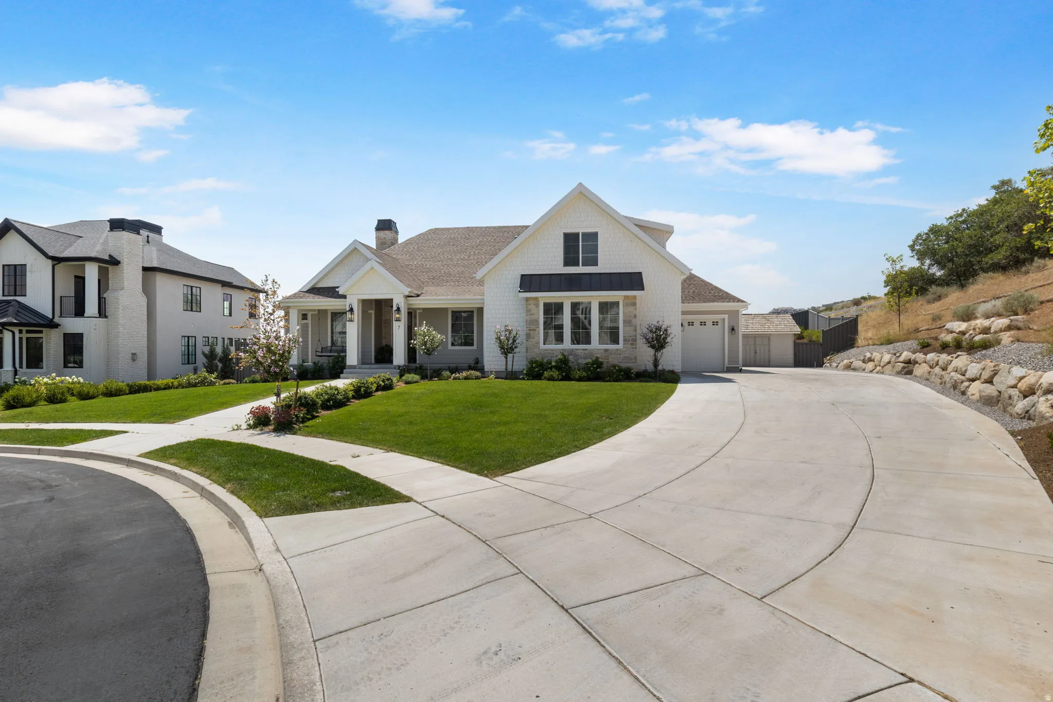 Contemporary exterior with white siding and dark trim accents, featuring a multi-car driveway, attached garage, and a landscaped front yard with a stone retaining wall