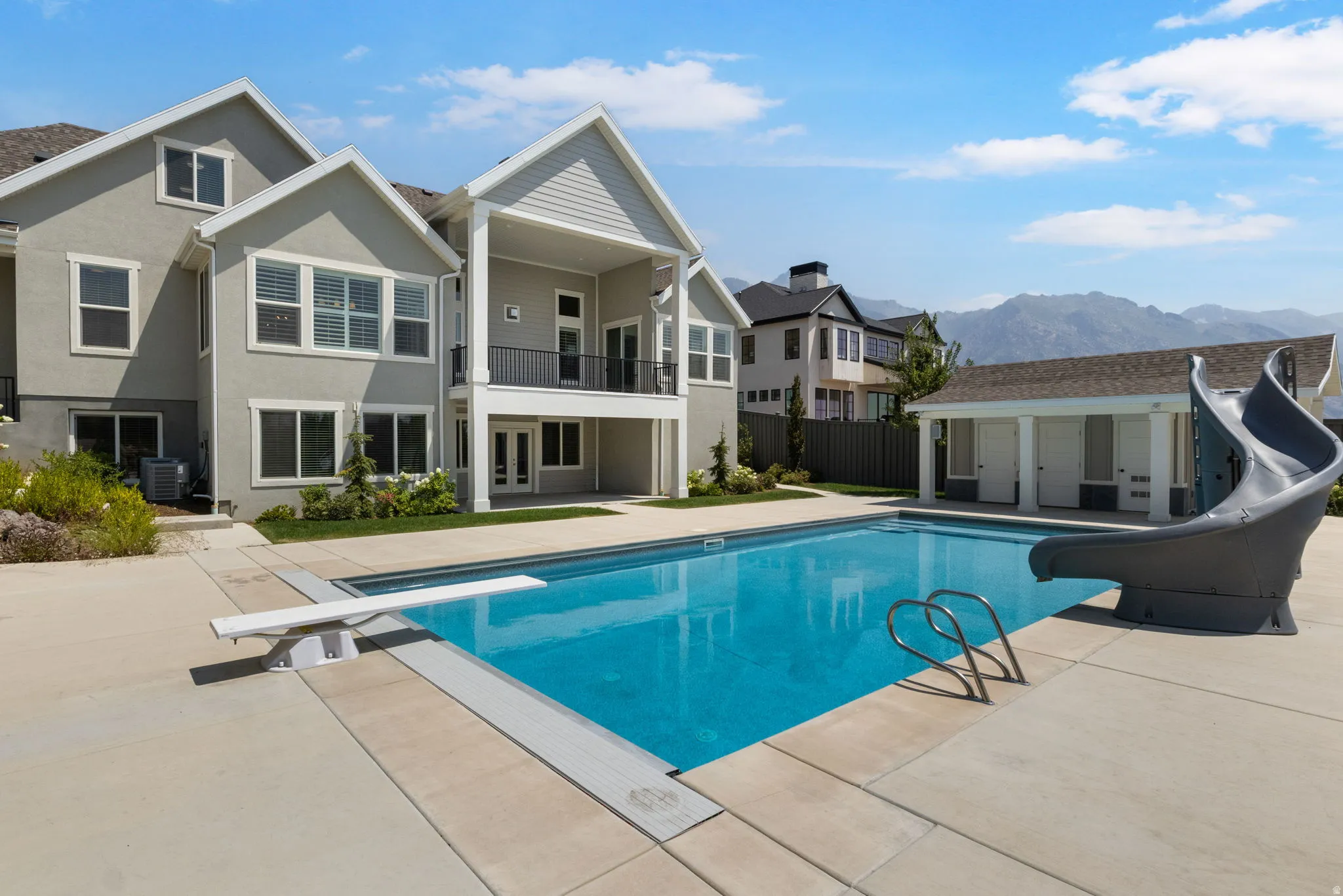 Expansive rear exterior featuring a swimming pool, concrete decking, diving board, and pool slide