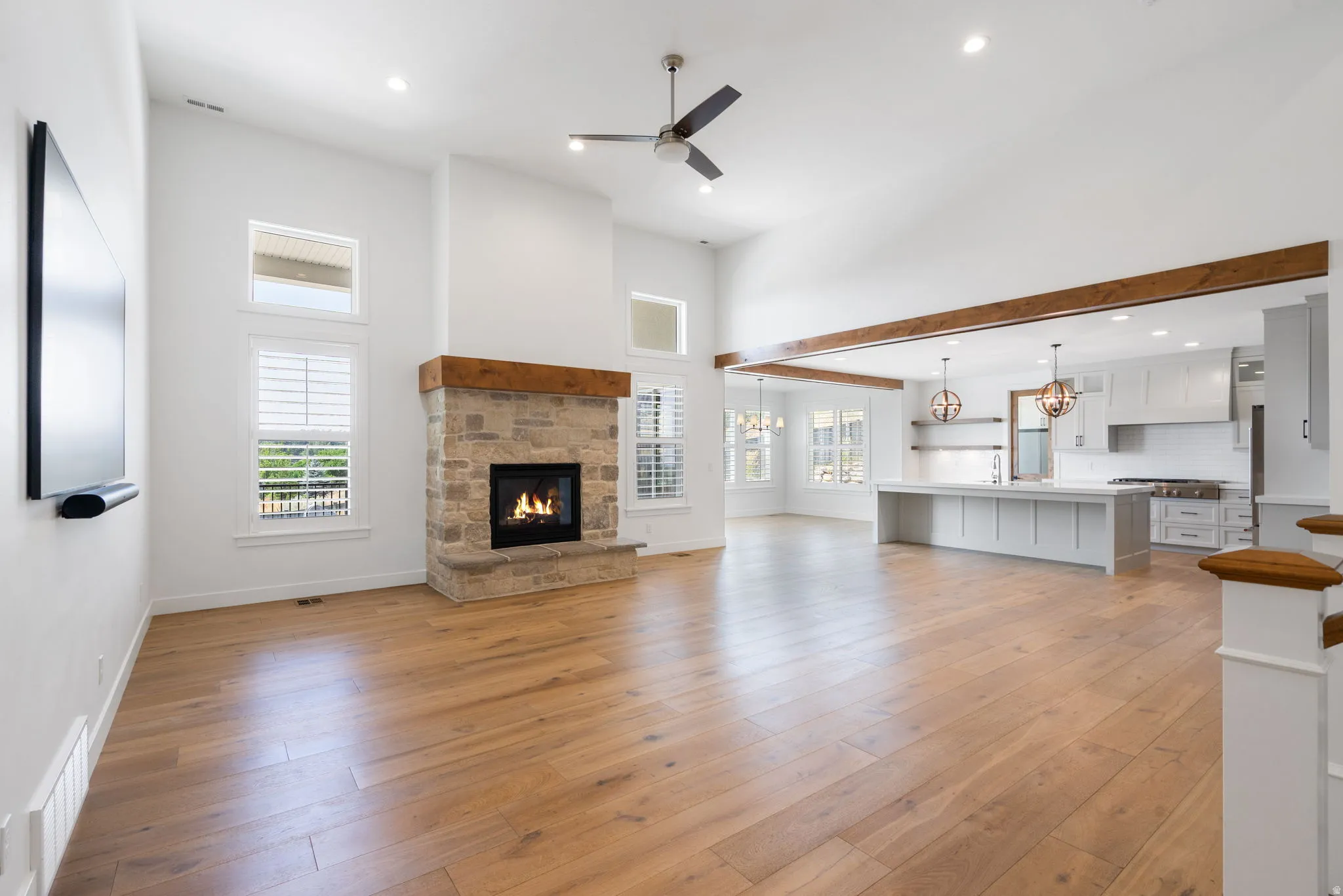 Open-concept great room featuring a stone fireplace with a wood mantle, wood-finish flooring, and high vaulted ceilings
