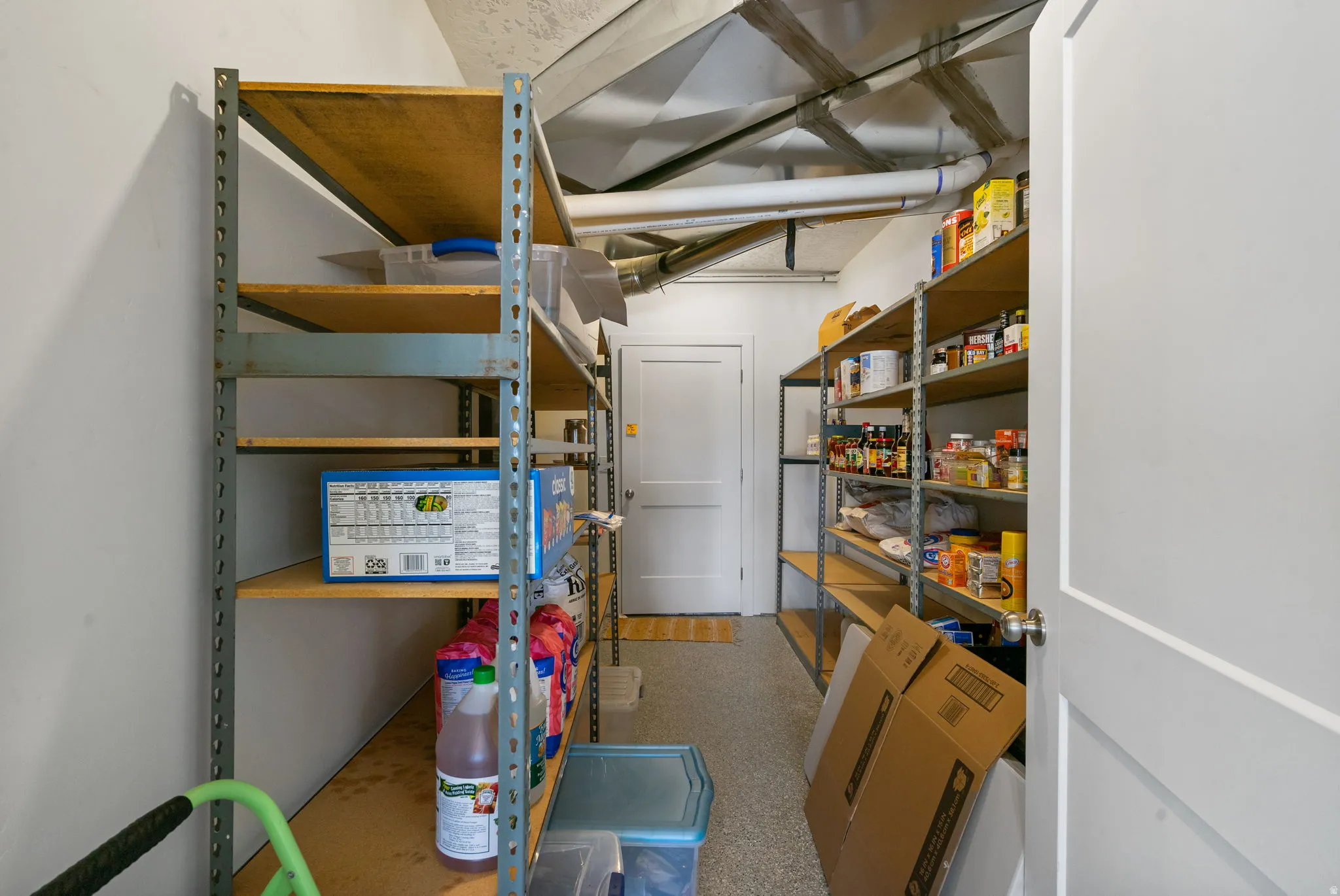 Storage room featuring multiple metal shelving units, a white door, and exposed ductwork