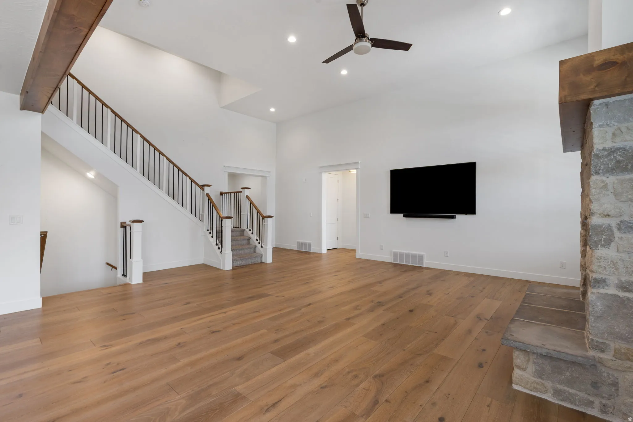 Vaulted ceiling with a ceiling fan, wood-finish flooring, stone-clad fireplace, and a staircase with wood handrails