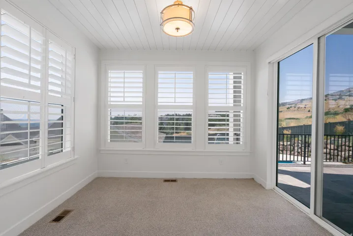Carpeted interior with multiple windows featuring white plantation shutters, white paneled ceiling, and a ceiling-mounted light fixture