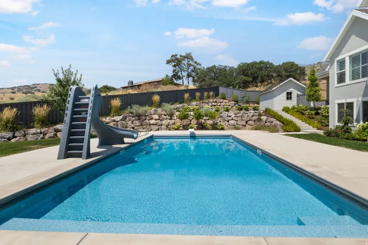 Outdoor swimming pool with integrated steps, concrete surround, adjacent slide, and terraced landscaping