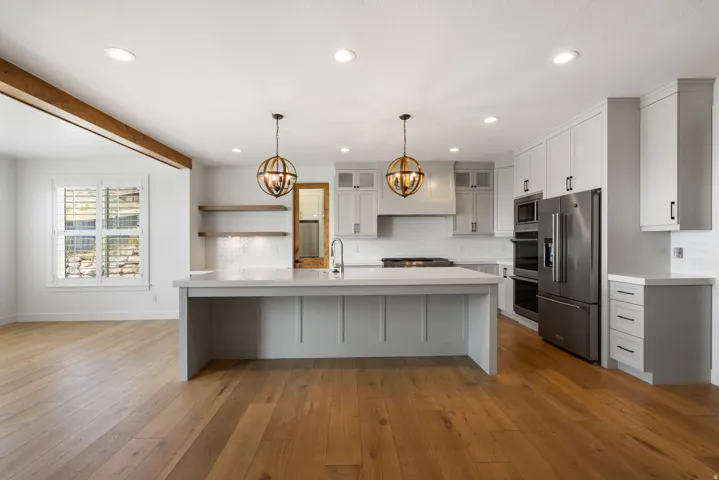 Open-concept kitchen with a large central island, light wood-finish flooring, white shaker-style cabinetry, and stainless steel appliances