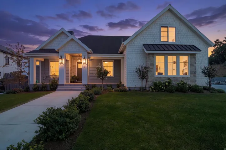 Gable roofline, white horizontal siding, stone facade accents, covered front porch, and mature landscaping