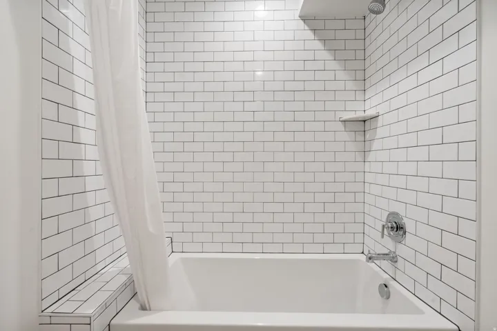 White subway tile surround with contrasting grout, built-in corner shelf, and a polished chrome shower fixture set