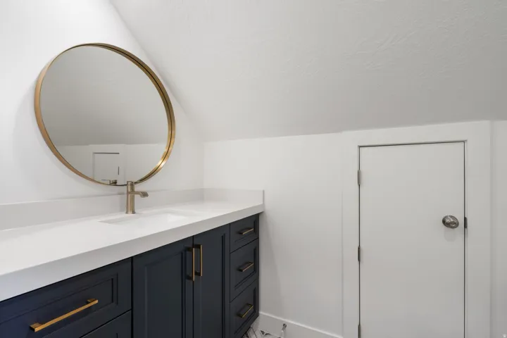 Vanity with a white countertop and integrated sink, gold-tone faucet, and dark blue cabinetry with gold-tone hardware