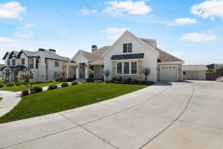 White siding exterior with a partial stone facade, a two-car garage, a concrete driveway, and a manicured lawn