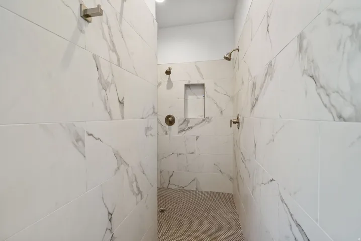 Shower enclosure with large format stone-finish tile, dual shower heads, integrated wall niche, and mosaic tile flooring