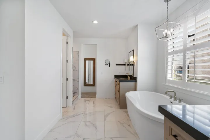 Freestanding soaking tub, walk-in shower with tile surround, double vanity with dark countertops, and large format floor tiling