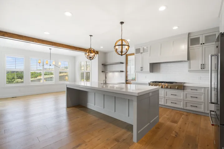 Hardwood flooring throughout, featuring a kitchen island with stone countertop, light gray cabinetry, and a subway tile backsplash