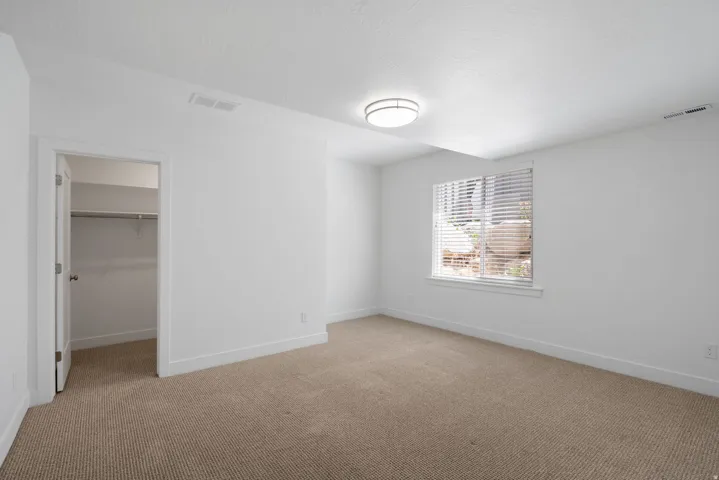 White painted walls, neutral carpet flooring, recessed window with horizontal blinds, flush mount ceiling light, and a closet with a built-in rod