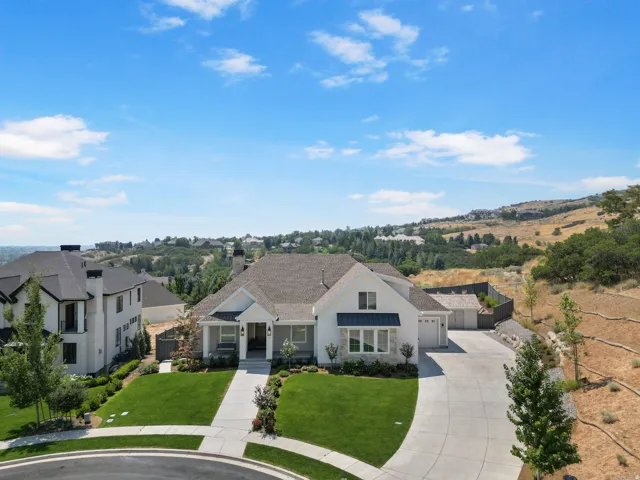White exterior with dark roof, manicured front lawn, curved concrete driveway, and attached garage