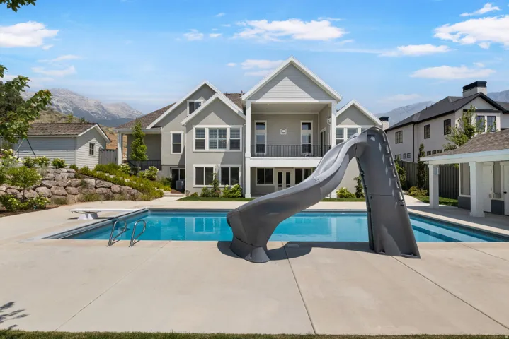 Expansive backyard featuring an in-ground swimming pool with an attached slide, a diving board, and a surrounding concrete patio