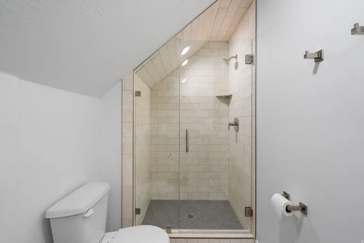 Glass-enclosed shower with subway tile surround, tile flooring, and integrated corner shelf