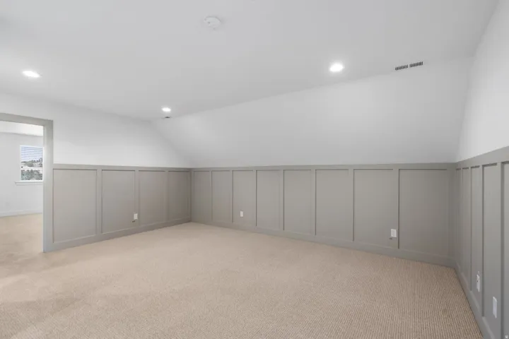 Sloped ceiling room featuring carpet flooring and board and batten wainscoting