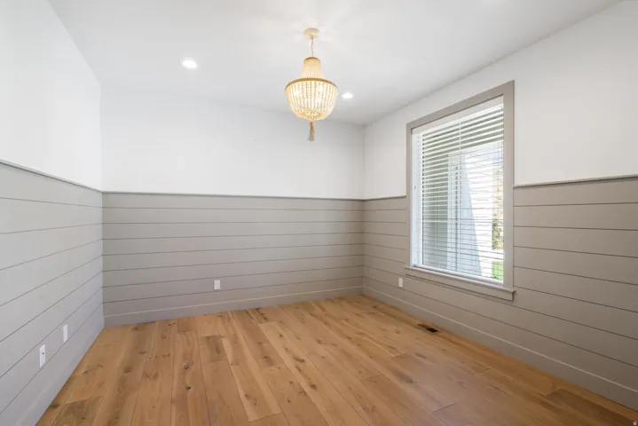 Wood-finish flooring, accent shiplap walls, recessed ceiling lighting, single window, and a decorative chandelier