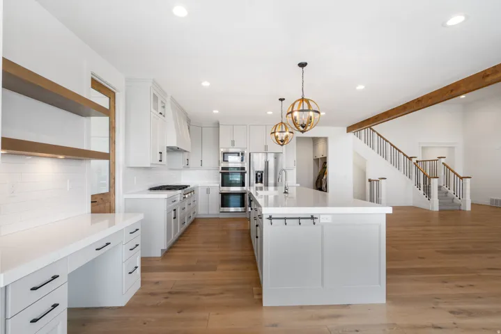 Gourmet kitchen featuring a center island with pendant lighting, stainless steel appliances, light wood-finish flooring, and a staircase with wood railings