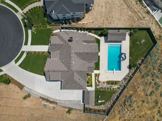 Expansive property featuring a multi-gabled roofline, concrete driveway, manicured lawns, a rectangular swimming pool with an attached spa, and a pool house