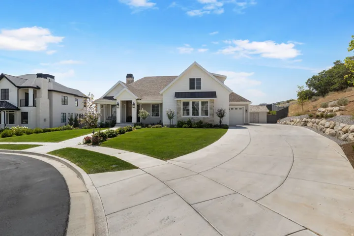 Contemporary exterior with white siding and dark trim accents, featuring a multi-car driveway, attached garage, and a landscaped front yard with a stone retaining wall