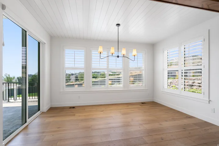 Wood-finish flooring, white shiplap ceiling, contemporary chandelier, plantation shutters, and sliding glass door