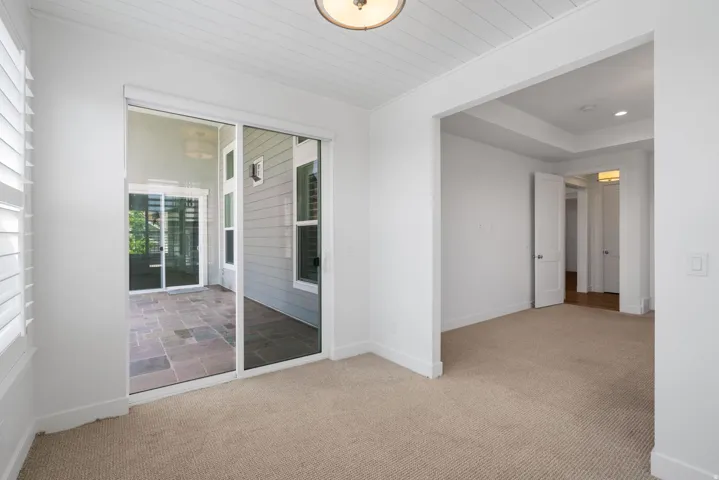 Bright primary bedroom with sliding glass doors opening to outdoor patio, neutral carpet flooring, recessed ceiling lighting, and direct access to hallway with additional room entries