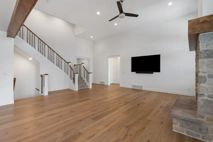 Vaulted ceiling with a ceiling fan, wood-finish flooring, stone-clad fireplace, and a staircase with wood handrails